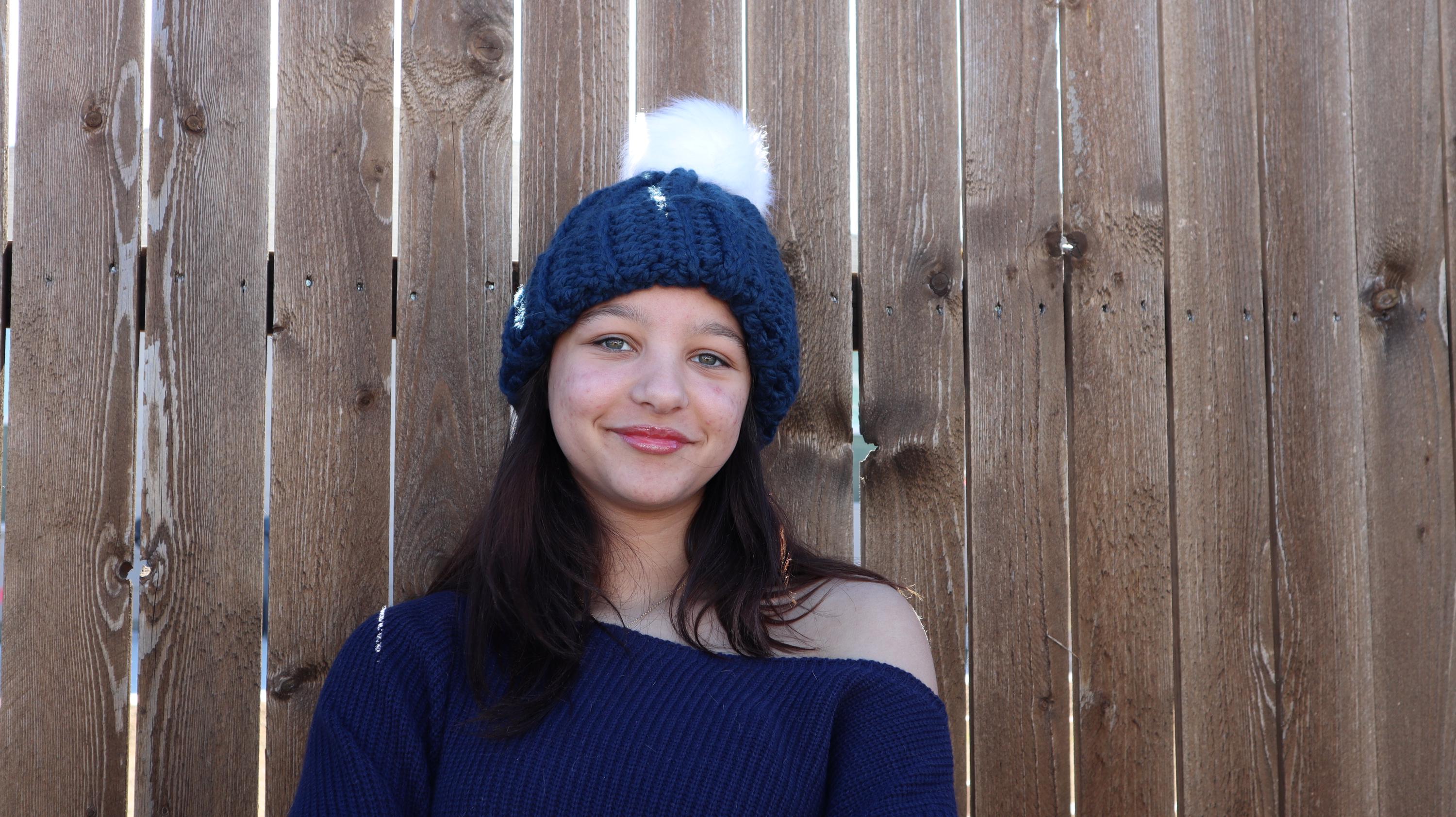 Model wearing blue crocheted beanie with white faux fur pom