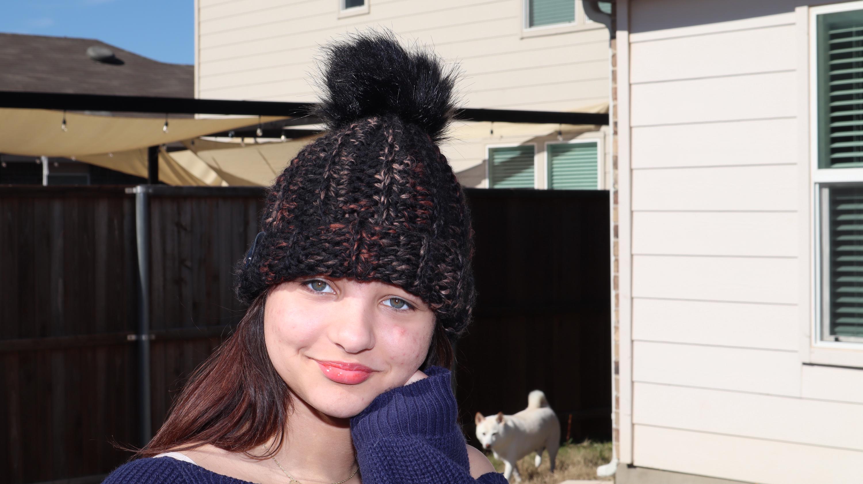 Model wearing brown, orange, and tan crocheted beanie with dark brown faux fur pom-pom