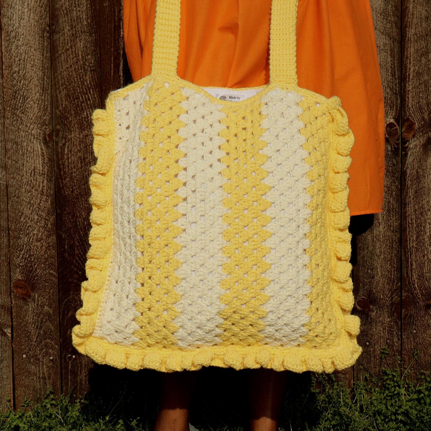 Picture of crochet, granny stitch bag with ruffles, while outdoors with fence and orange dress in the background