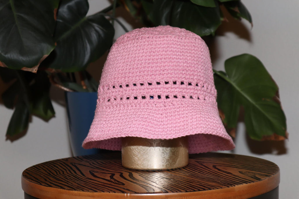 Bucket hat in rose with green plants in the background